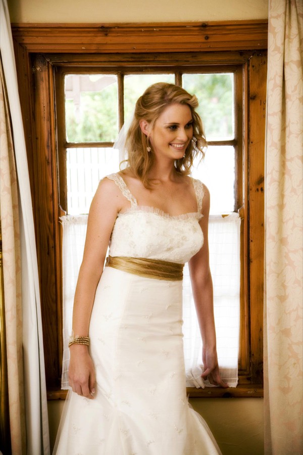 Bride in a fitted ivory gown with a gold silk sash, photographed in soft window light