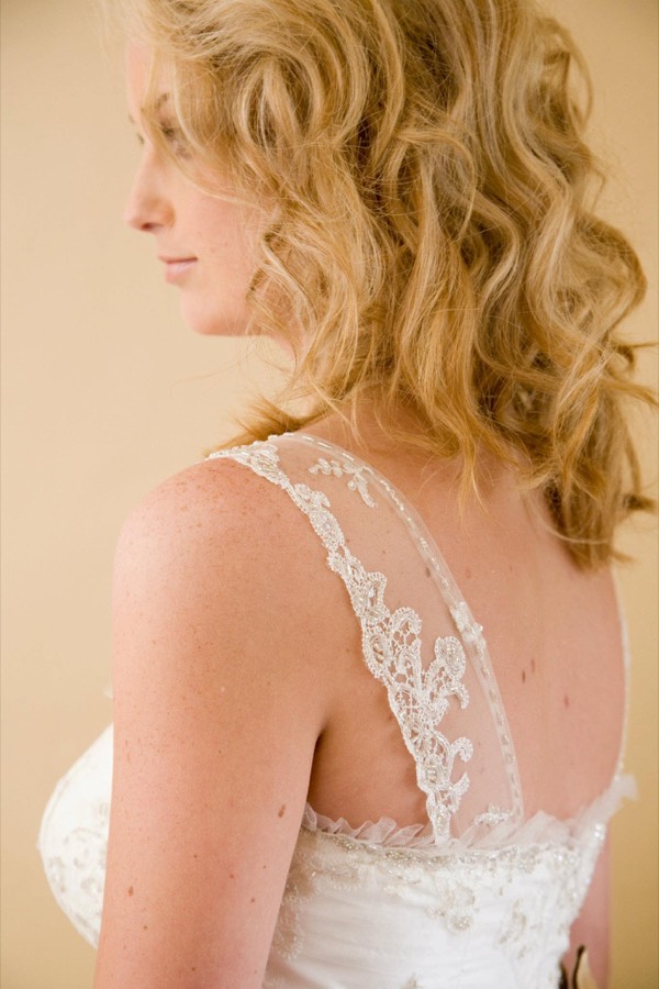 Close detail of a bride's shoulder and the scalloped lace edge of a low back